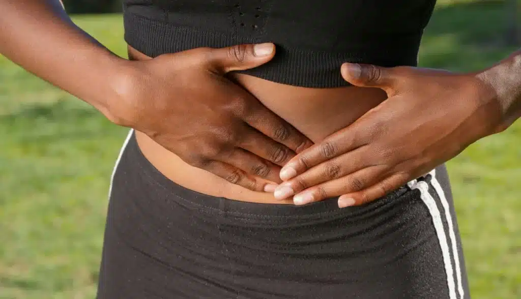 Mãos segurando a barriga, indicando possível dor abdominal crônica. A imagem transmite a sensação de desconforto e sofrimento.