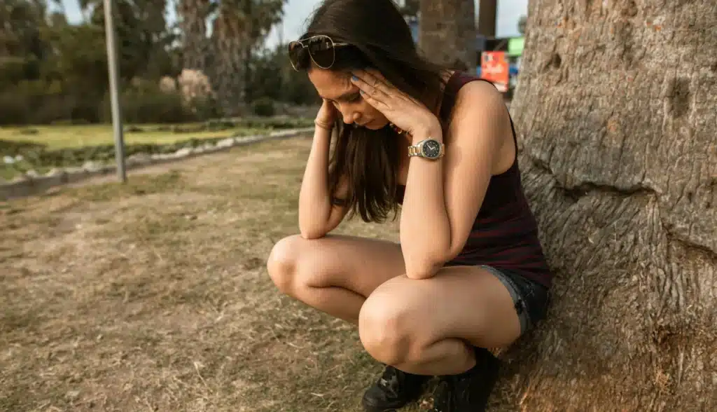 Mulher com semblante triste, cabeça baixa e mãos entrelaçadas, retratando sentimentos de ansiedade profunda e vulnerabilidade. Inclui a mensagem: "Como Controlar a Ansiedade em 5 Minutos